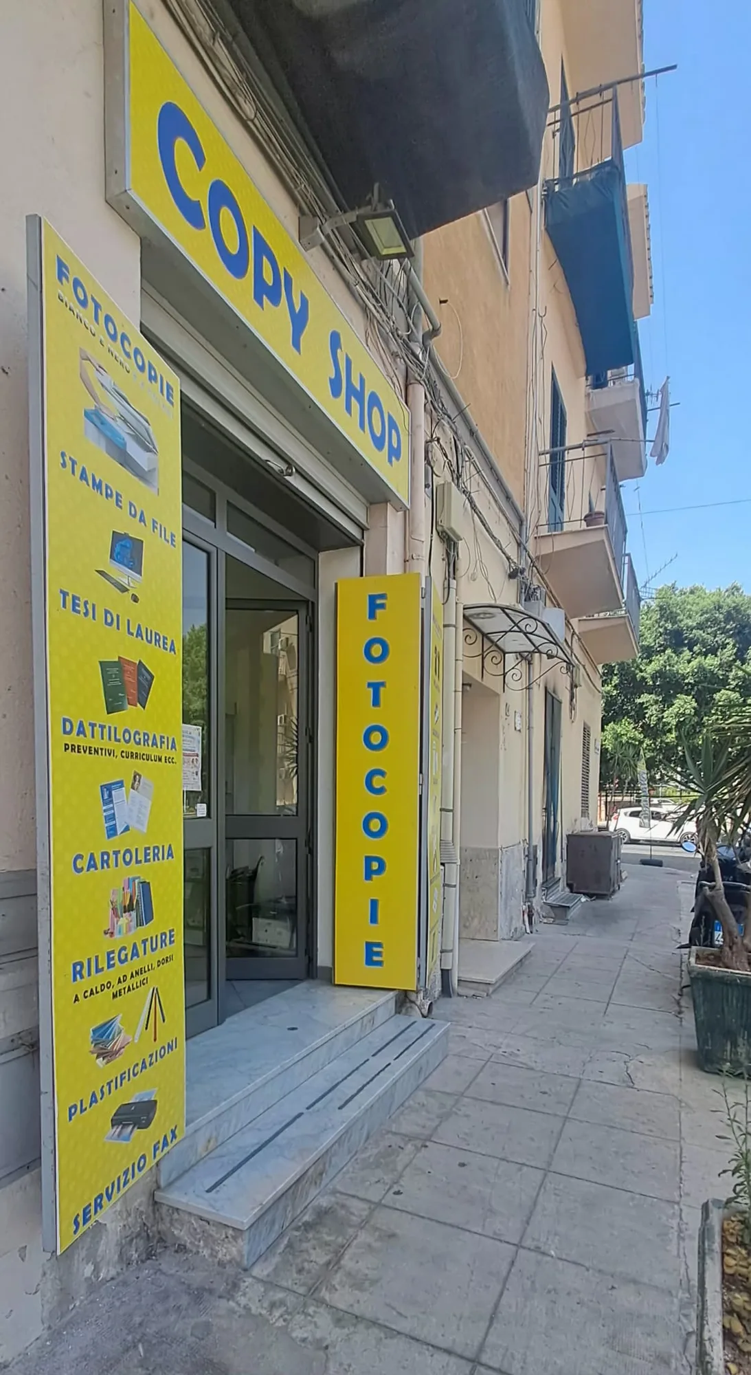 L'insegna gialla e blu COPY SHOP sopra l'ingresso e il totem FOTOCOPIE, in Via Emilio D'Angelo a Palermo