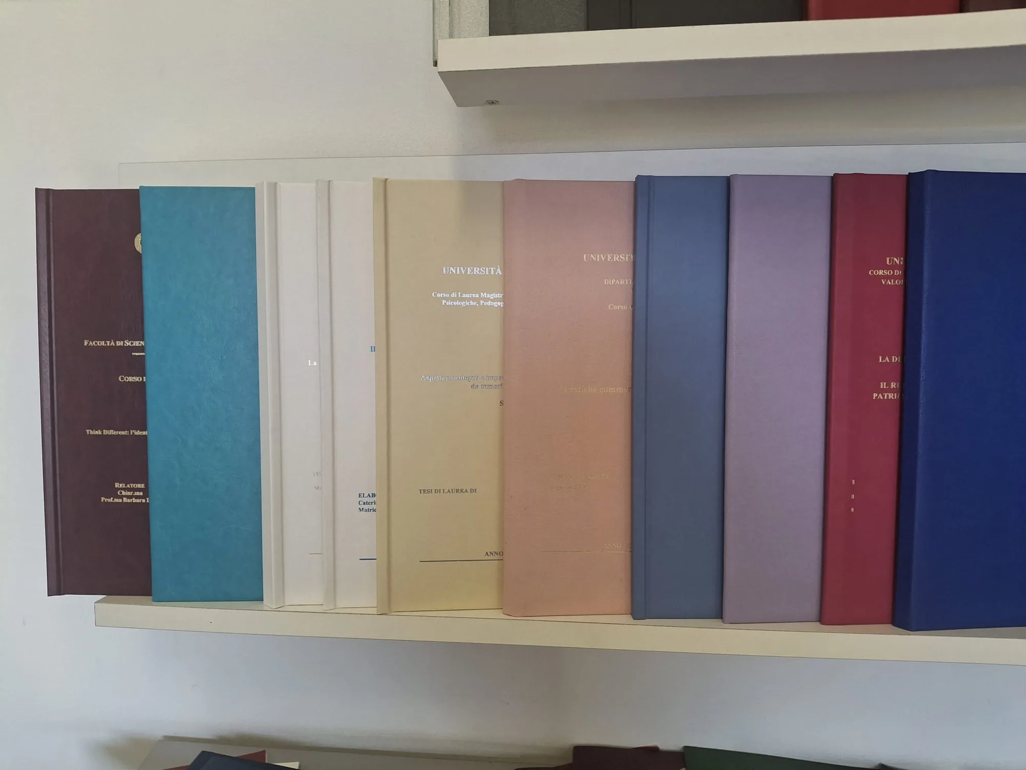 Tesi di laurea rilegate in pelle di colori diversi, appoggiate una accanto all'altra sul bancone