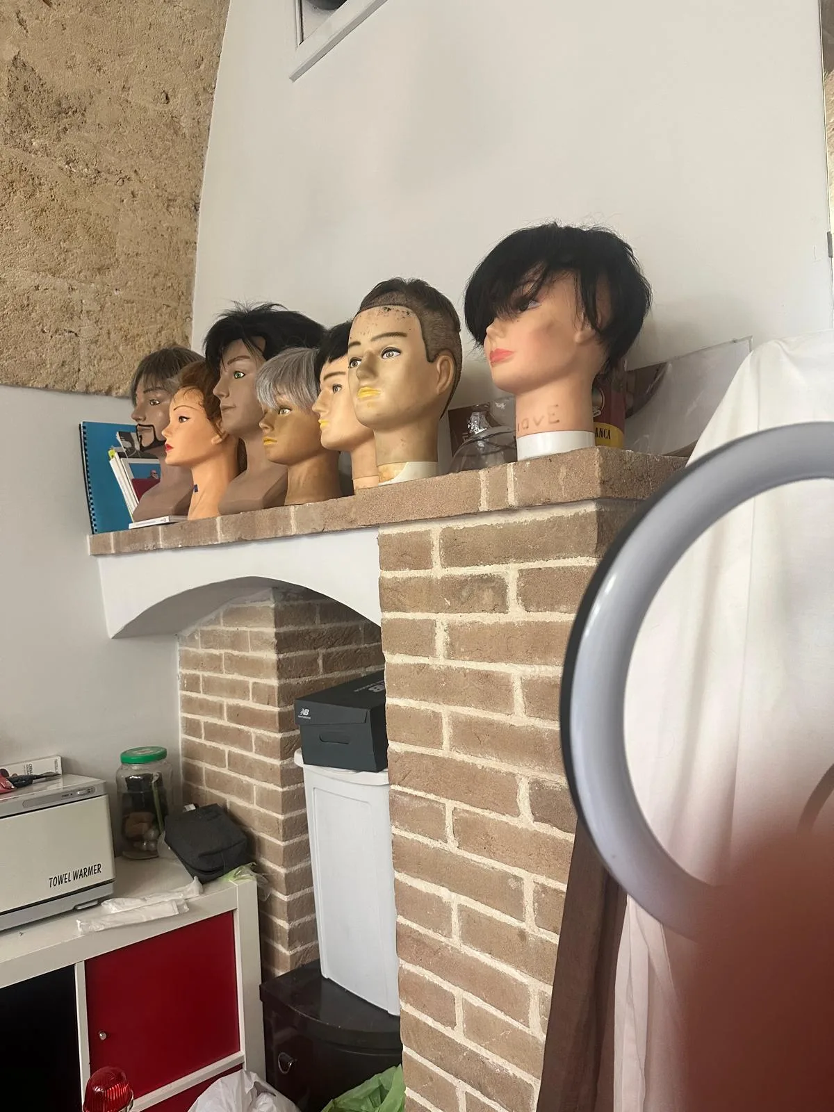 Teste da lavoro allineate sulla mensola in mattoni del salone, ognuna con una patch di capelli di colore diverso